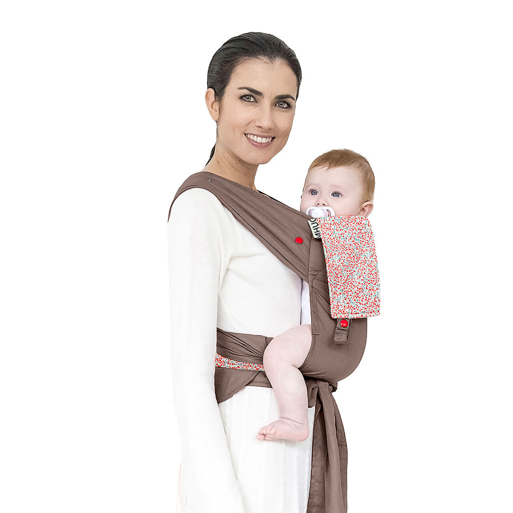 portabebè mhug mei tai collezione fantasia modello Romantic fondo di base tortora con bavero fantasia fiorellini rossi bottoni a pressione rossi  indossato da modella con bambina di sei mesi circa in posizione canguro in ripresa trequarti