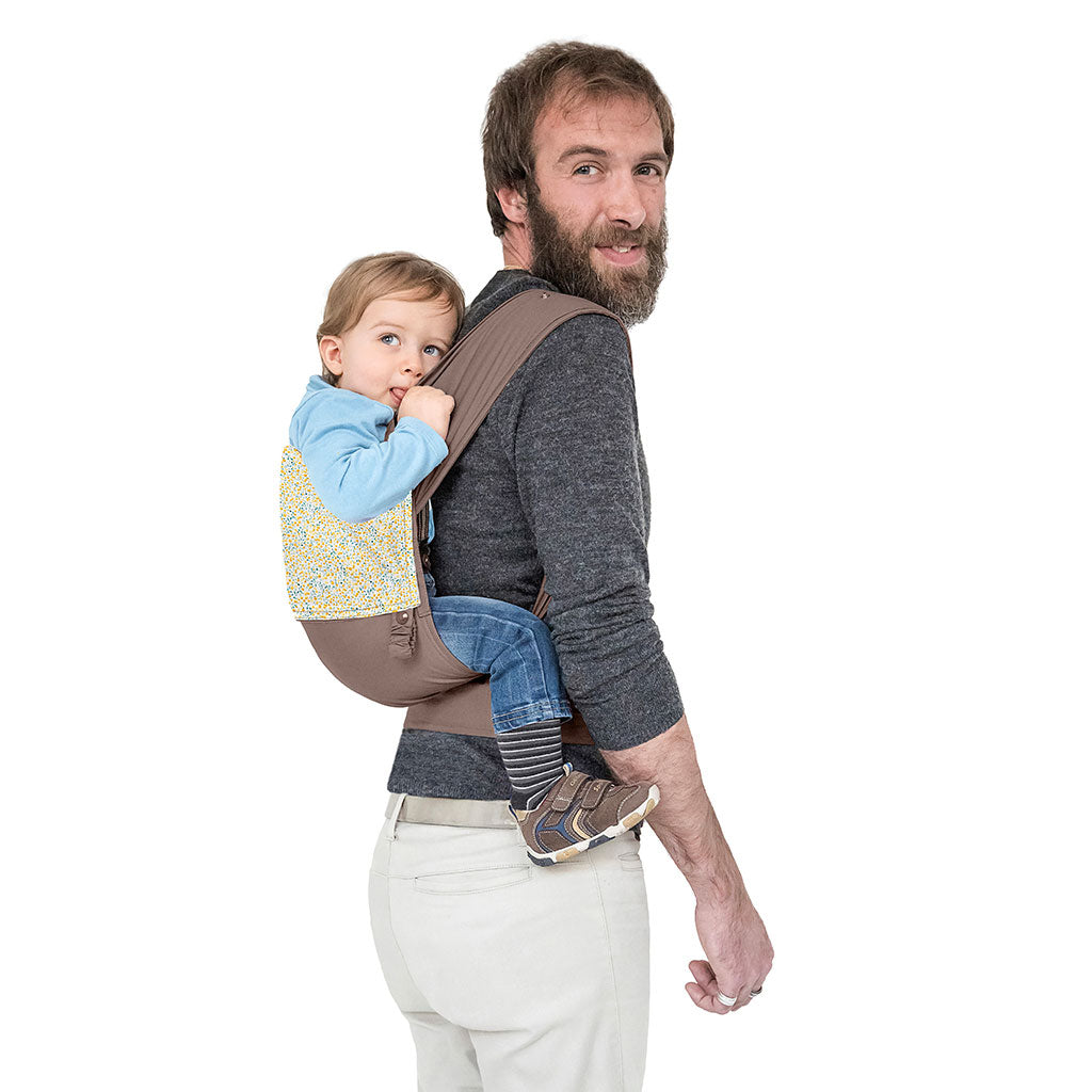 portabebè mhug mei tai collezione fantasia modello Yellow Romantic fondo di base tortora con bavero fantasia fiorellini gialli bottoni a pressione tortora indossato da modello con bambino di dodici mesi circa in posizione zainetto in ripresa di trequarti di spalle